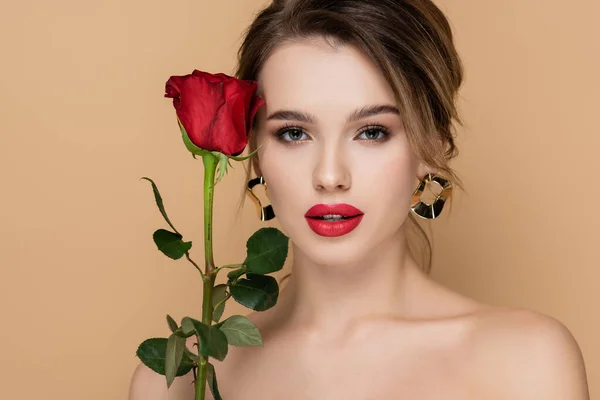 Charmante Frau mit roten Lippen und frischer Rose, die isoliert auf Beige in die Kamera blickt — Stockfoto