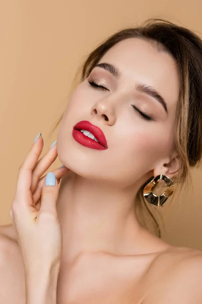 Vista de cerca de la mujer joven con labios rojos tocando la cara aislada en beige - foto de stock