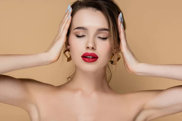 Young woman with closed eyes and bare shoulders touching hair isolated on beige — Stock Photo