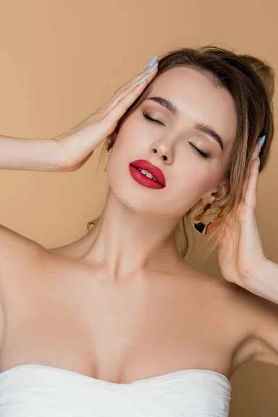 Mujer encantadora con los ojos cerrados y hombros desnudos tocando pelo aislado en beige - foto de stock