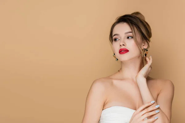 Pretty young woman in strapless top and golden earrings looking away isolated on beige — Stock Photo