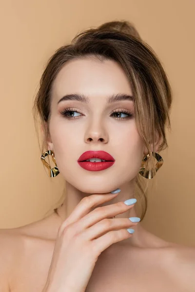Hübsche Frau mit Make-up und goldenen Ohrringen schaut vereinzelt auf beige — Stockfoto