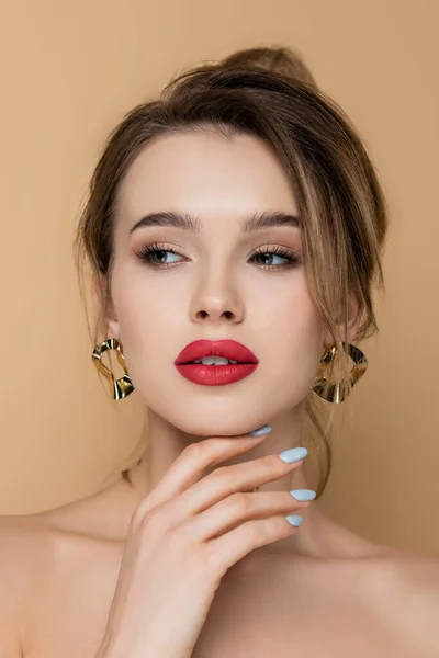 Jolie femme avec maquillage et boucles d'oreilles dorées regardant loin isolé sur beige — Photo de stock