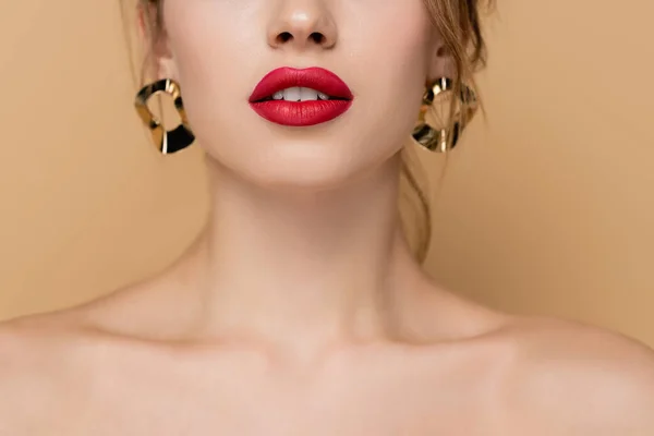 Vista de cerca de la mujer recortada con labios rojos y pendientes de oro aislados en beige - foto de stock