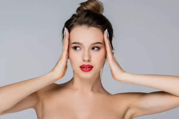 Young and pretty woman with naked shoulders touching head while looking away isolated on grey — Stock Photo