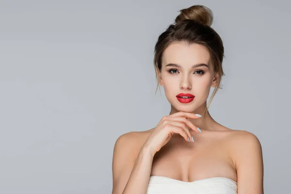 Mujer joven y bonita en la parte superior sin tirantes mirando a la cámara aislada en gris - foto de stock