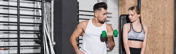 Young trainer with dumbbell near sportswoman in sports center, banner — Stock Photo