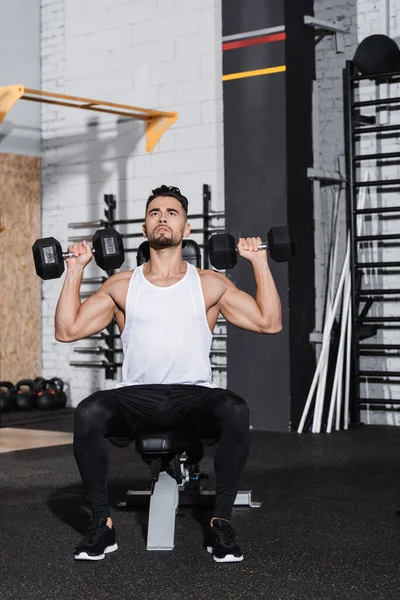 Joven deportista haciendo ejercicio con mancuernas en el centro deportivo - foto de stock