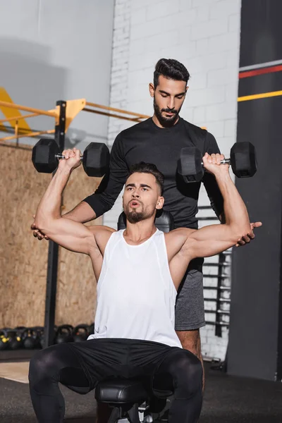 Arabe entraîneur debout près du sportif avec haltères dans la salle de gym — Photo de stock