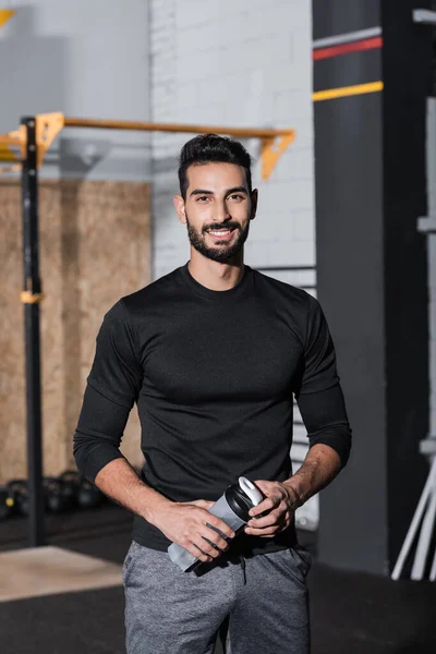 Smiling arabian sportsman holding sports bottle in gym — Stock Photo