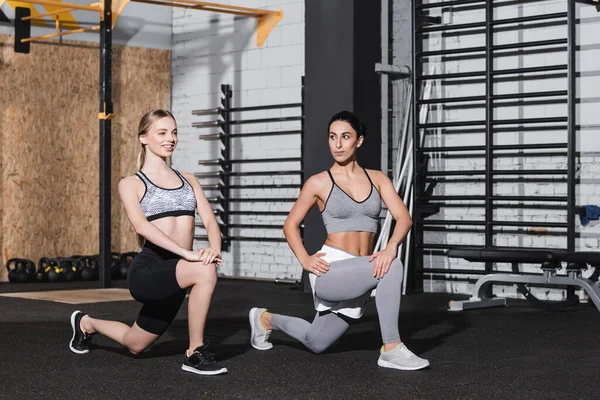 Sonrientes mujeres multiétnicas haciendo embestidas en el centro deportivo - foto de stock