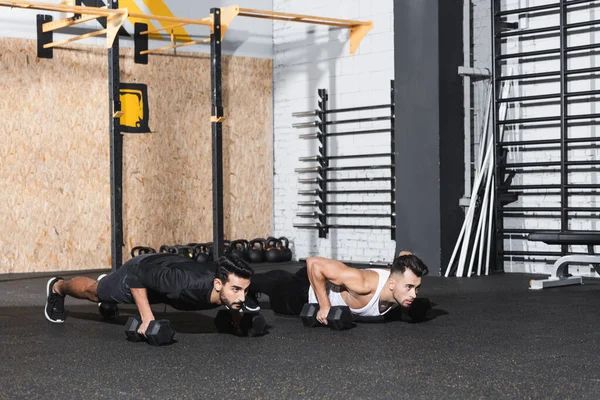 Desportistas multiétnicos fazendo press ups com halteres no ginásio — Fotografia de Stock