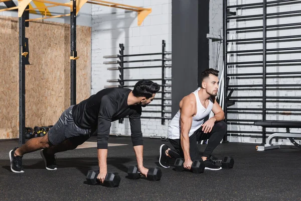 Sportsman holding dumbbell near arabian friend in gym — Stock Photo