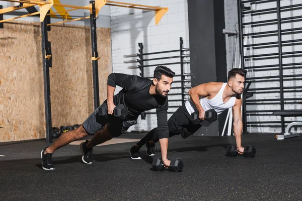 Interracial sportsmen training with dumbbells in sports center — Stock Photo