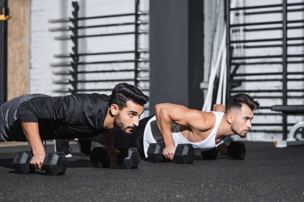 Young arabian sportsman doing press ups near friend with dumbbells in gym — Stock Photo