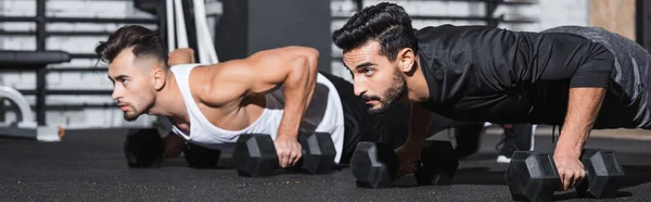 Arabian man working out with dumbbells near sportsman in gym, banner — Stock Photo