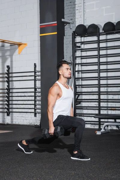 Sportsman doing lunges with dumbbells in sports center — Stock Photo