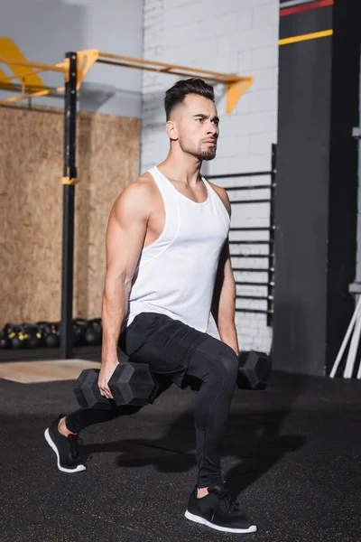 Jovem desportista segurando halteres enquanto faz lunges no ginásio — Fotografia de Stock