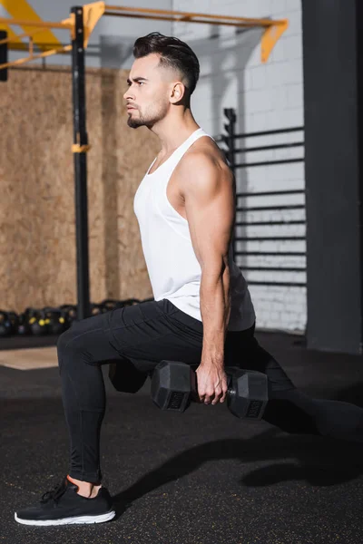 Sportsman doing lunges and holding dumbbells in sports center — Stock Photo