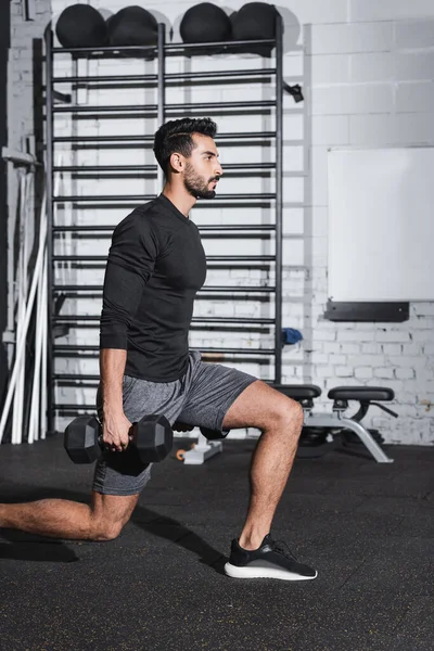 Seitenansicht muslimischer Sportler mit Hanteln beim Ausfallschritt im Sportzentrum — Stockfoto