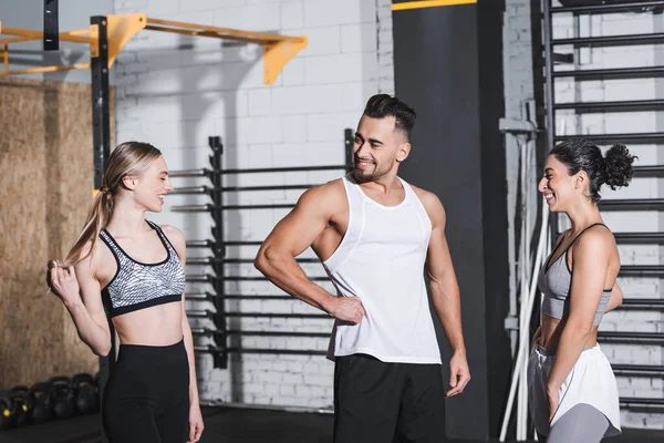 Positive sportsman standing near multiethnic sportswomen in gym — Stock Photo