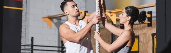 Multiethnic people in sportswear standing near climbing rope in gym, banner — Stock Photo