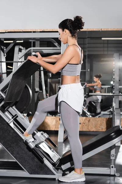 Side view of middle east sportswoman training with leg press machine in gym — Stock Photo