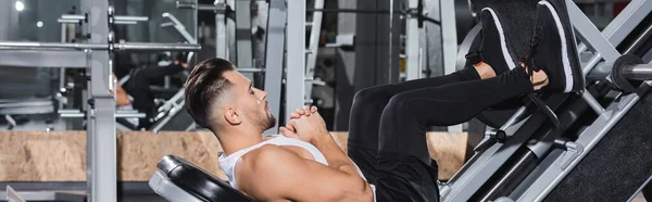 Side view of sportsman working out with leg press machine in gym, banner — Stock Photo