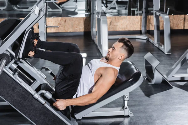 Vista lateral del entrenamiento de deportista deportivo con máquina de prensa de piernas en el gimnasio - foto de stock