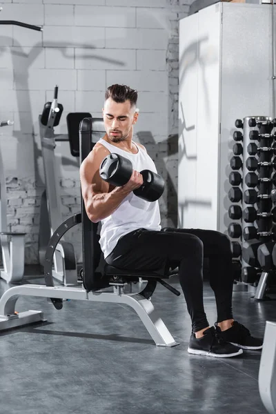 Jeune sportif regardant les muscles tout en s'entraînant avec haltère dans la salle de gym — Photo de stock