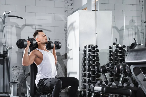 Jeune homme en tenue de sport soulevant des haltères dans la salle de gym — Photo de stock