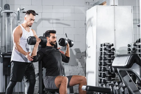 Trainer helping arabian sportsman with dumbbells in sports center — Stock Photo