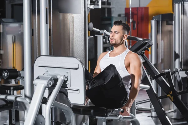 Sportsman em treinamento sportswear na perna imprensa máquina perto de equipamentos esportivos no ginásio — Fotografia de Stock