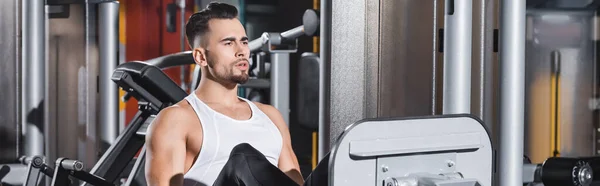 Athletic sportsman training on leg press machine in sports center, banner — Stock Photo