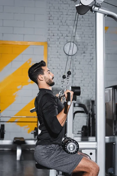 Vue latérale de l'entraînement sportif musulman avec une machine de traction latérale dans le centre sportif — Photo de stock