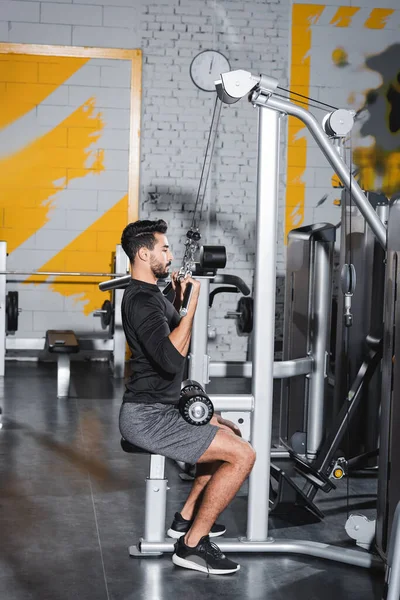 Vue latérale de l'entraînement de l'homme arabe avec machine de traction lat dans la salle de gym — Photo de stock