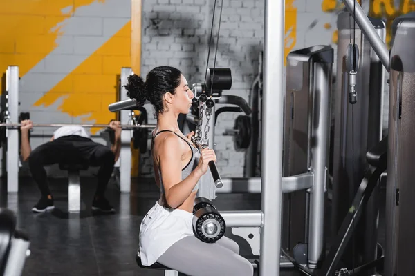 Mujer de Oriente Medio con entrenamiento de mancuerna en la máquina de extracción de lat en el gimnasio - foto de stock