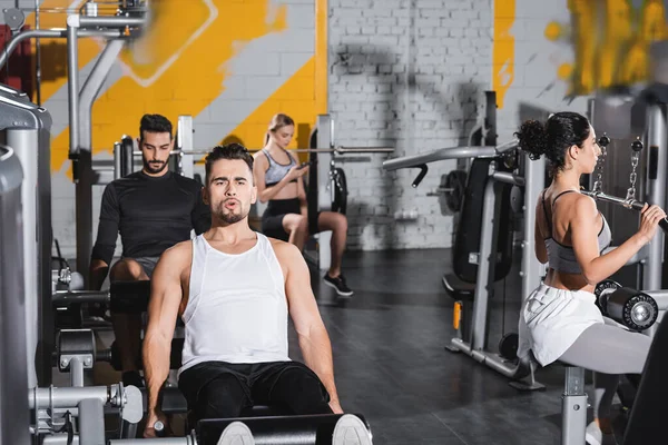 Allenamento sportivo sulla macchina arricciacapelli gamba vicino a persone interrazziali nel centro sportivo — Foto stock