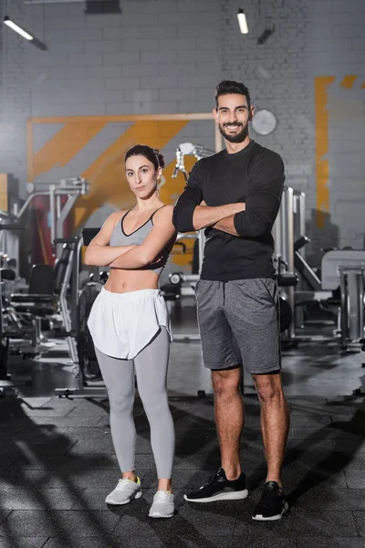 Positive muslim sportsman crossing arms near middle east sportswoman in gym — Stock Photo