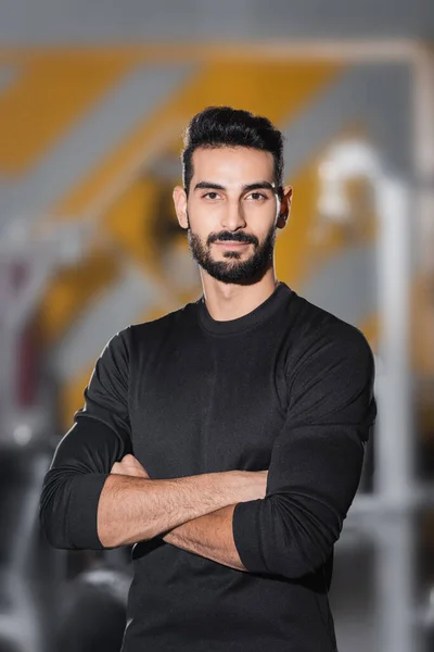 Un sportif arabe barbu regardant une caméra dans un centre sportif flou — Photo de stock