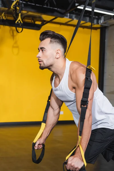 Giovane sportivo tirando cinghie di sospensione in palestra — Foto stock