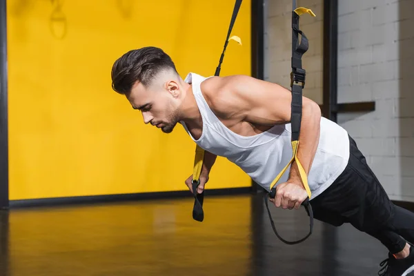 Athletic man working out with suspension straps in gym — Stock Photo