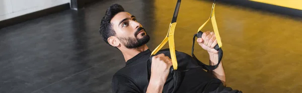 Bearded arabian man working out with suspension straps in sports center, banner — Stock Photo