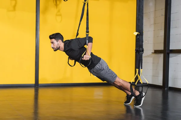 Side view of muslim sportsman working out with suspension straps in sports center — Stock Photo