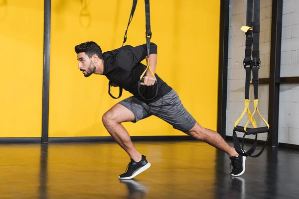 Vista lateral del deportista musulmán haciendo ejercicio con correas de suspensión en el gimnasio - foto de stock
