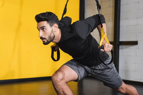 Esportista árabe barbudo puxando tiras de suspensão no ginásio — Fotografia de Stock