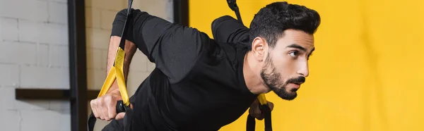 Young arabian sportsman pulling suspension straps in sports center, banner — Stock Photo