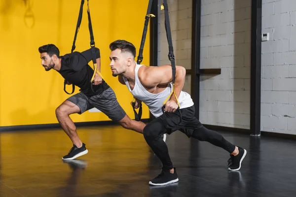 Athletic interracial sportsmen training with suspension straps in sports center — Stock Photo