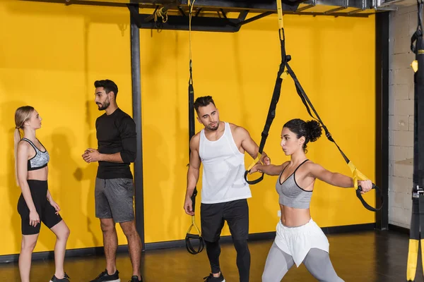 Middle east sportswoman pulling suspension straps near friends in gym — Stock Photo