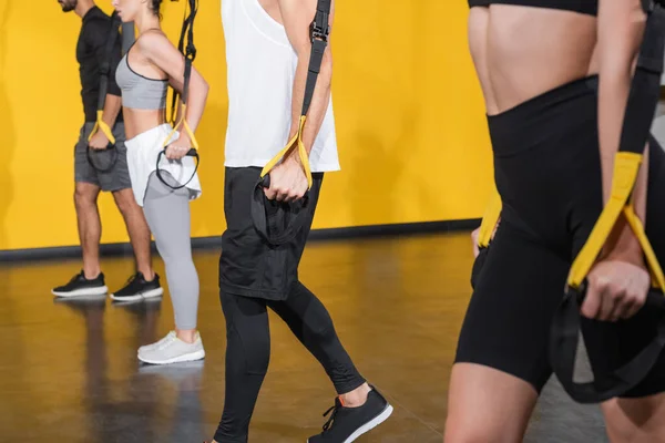 Cropped view of people in sportswear holding suspension straps in gym — Stock Photo